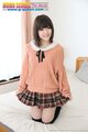 Kneeling on bed playing with the hem of her plaid short skirt short hair in orange sweater